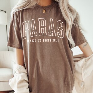 May include: An oversized brown t-shirt with the text "PARAS MAKE IT POSSIBLE" in white. The shirt is made of a soft, comfortable material.