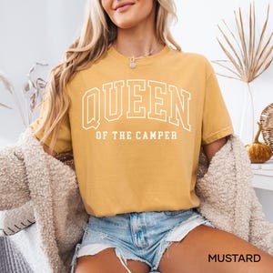 May include: A mustard yellow t-shirt with the text "QUEEN OF THE CAMPER" in white.