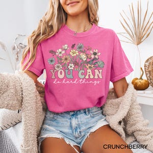 May include: A pink t-shirt with a floral design and the text "YOU CAN do hard things" in a retro font.