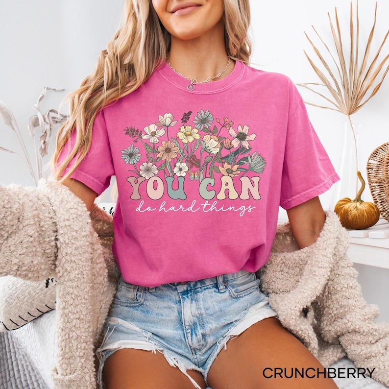 May include: A pink t-shirt with a floral design and the text "YOU CAN do hard things" in a retro font.