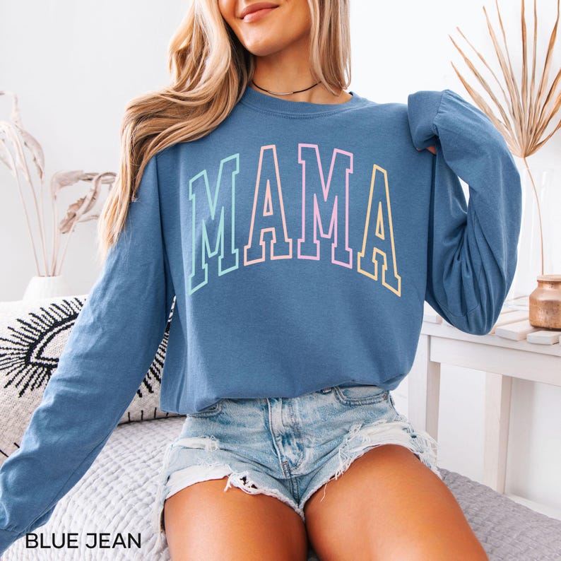 May include: A blue long-sleeved shirt with the word "MAMA" printed in rainbow colors. The shirt is cropped and has a relaxed fit.