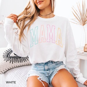 May include: White long-sleeved shirt with the word "MAMA" in rainbow colors.
