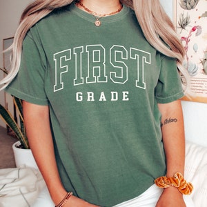 May include: A green t-shirt with the text "FIRST GRADE" in white outlined letters.