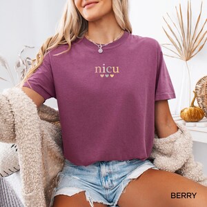 May include: Berry-colored t-shirt with the word "nicu" embroidered in gold letters above three small gold hearts. The shirt is short-sleeved and has a relaxed fit. The word "BERRY" is printed in white at the bottom of the image.