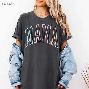 May include: A dark gray t-shirt with the word "MAMA" printed in rainbow colors. The shirt has a relaxed fit and is made of a soft, comfortable fabric.