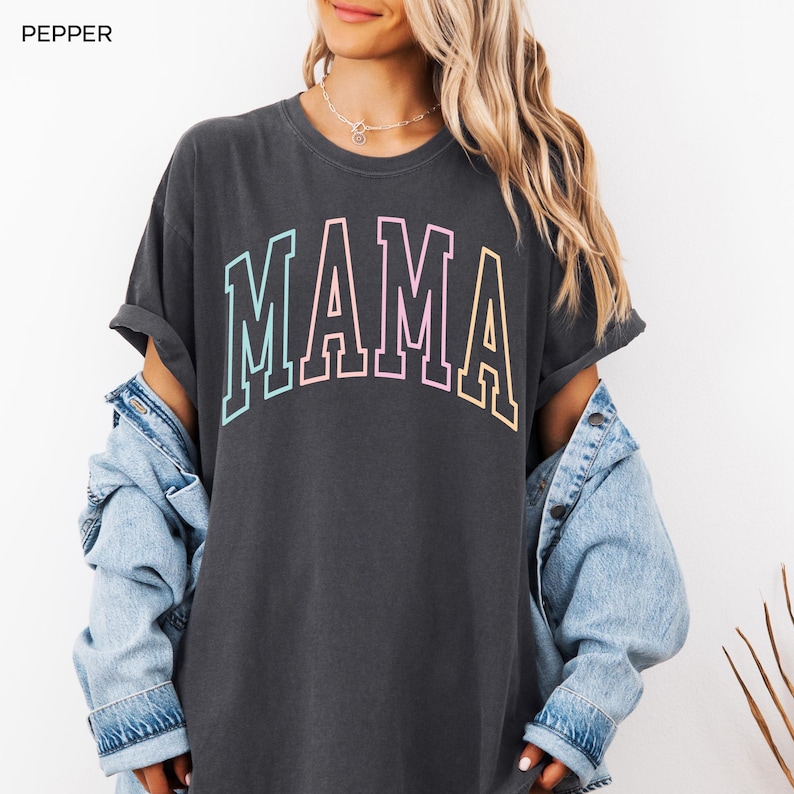 May include: A dark gray t-shirt with the word "MAMA" printed in rainbow colors. The shirt has a relaxed fit and is made of a soft, comfortable fabric.