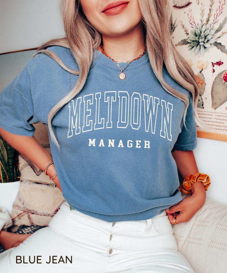 May include: A blue jean t-shirt with white text that reads "MELTDOWN MANAGER".