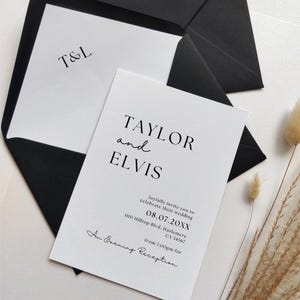 Peut inclure: Ensemble de faire-part de mariage minimaliste. La carte principale, avec les noms "TAYLOR and ELVIS", la date, l'heure et le lieu, est posée sur une enveloppe noire. L'enveloppe intérieure affiche les initiales "T&L". Le design est épuré et moderne.