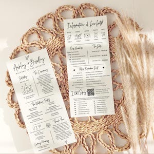 May include: Wedding stationery set with two cream-colored cards featuring black text and illustrations. One card lists the wedding details, while the other shares fun facts. The set is placed on a woven placemat with dried grass.
