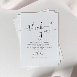 Peut inclure: Cartes de remerciement blanches avec un texte manuscrit élégant. Les cartes indiquent "merci" avec un symbole de cœur, suivi d'un message de gratitude et de la phrase "avec amour" des jeunes mariés.