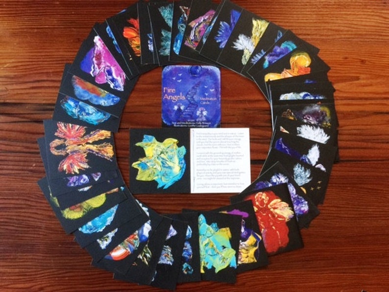 Puede incluir: Un juego de 32 cartas de meditaci&oacute;n Fire Angels. Las cartas presentan arte abstracto colorido con un fondo negro. Las cartas est&aacute;n dispuestas en un c&iacute;rculo alrededor de un peque&ntilde;o folleto titulado "Fire Angels Meditation Cards".