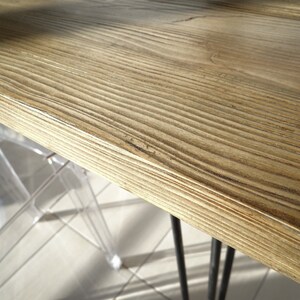 May include: Close-up of a light brown wooden table top with a natural wood grain pattern. The table top is smooth and polished. The table top is supported by black metal hairpin legs.