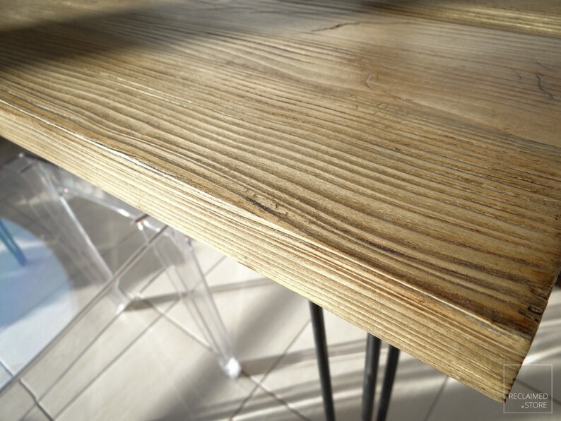 May include: Close-up of a light brown wooden table top with a natural wood grain pattern. The table top is smooth and polished. The table top is supported by black metal hairpin legs.