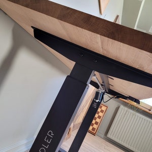 May include: A black electric standing desk frame with a wooden tabletop. The frame has a silver metal mechanism and a black label that says "DLEDER".