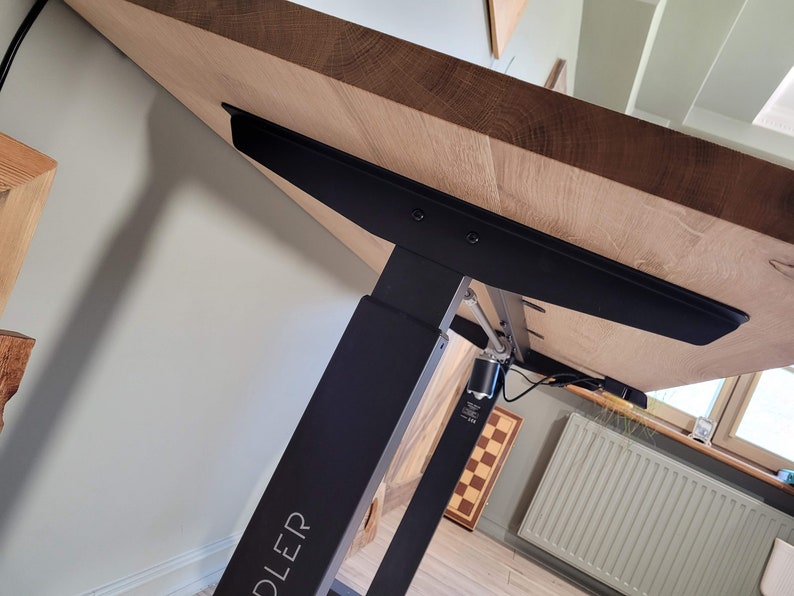 May include: A black electric standing desk frame with a wooden tabletop. The frame has a silver metal mechanism and a black label that says "DLEDER".