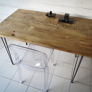 May include: A rustic wooden desk with black hairpin legs and a clear plastic chair. The desk has a natural wood finish and is made from reclaimed wood. The chair is a modern design and is made from clear acrylic.
