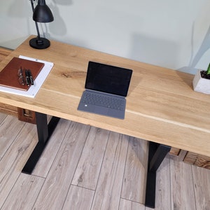 May include: A light wood desk with black metal legs. A laptop computer, a notebook, and a lamp are on the desk.