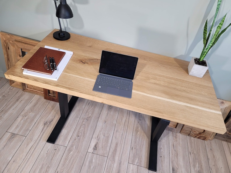 May include: A light wood desk with black metal legs. A laptop computer, a notebook, and a lamp are on the desk.