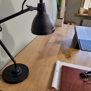 May include: A wooden desk with a black desk lamp, a laptop, a notebook, a leather-bound journal, two pens, and a pair of glasses.