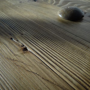 May include: Close-up of a wooden surface with a smooth, light brown finish. The wood has a natural grain pattern and a small, round stone is resting on the surface.