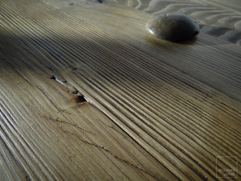 May include: Close-up of a wooden surface with a smooth, light brown finish. The wood has a natural grain pattern and a small, round stone is resting on the surface.