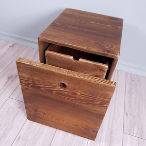 Pode incluir: Uma mesa de apoio de madeira com uma gaveta aberta. A mesa é feita de madeira marrom escura e tem um visual rústico. A gaveta tem um pequeno furo na frente.