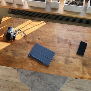 Może przedstawiać: Drewniane biurko z niebieskim etui na tablet, okularami, czarnym etui i czarnym smartfonem na górze.