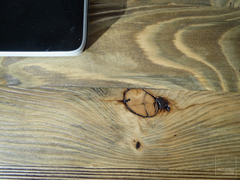 May include: Close-up of a light brown wooden surface with a knot in the center. The wood has a natural grain pattern and is slightly weathered.