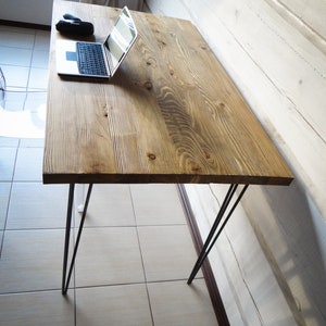 May include: A wooden desk with a natural finish and black hairpin legs. A laptop computer is on the desk.
