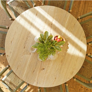 May include: A round wooden table with a light wood finish and a green plant in the center. The table is surrounded by six green wicker chairs.