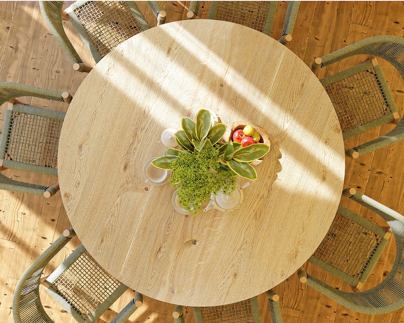 May include: A round wooden table with a light wood finish and a green plant in the center. The table is surrounded by six green wicker chairs.