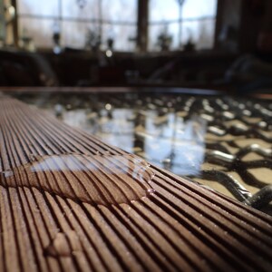 May include: A close-up of a wooden surface with a water droplet on it. The surface is made of thin, parallel strips of wood, creating a striped pattern. The water droplet is reflecting the light, creating a shimmering effect.