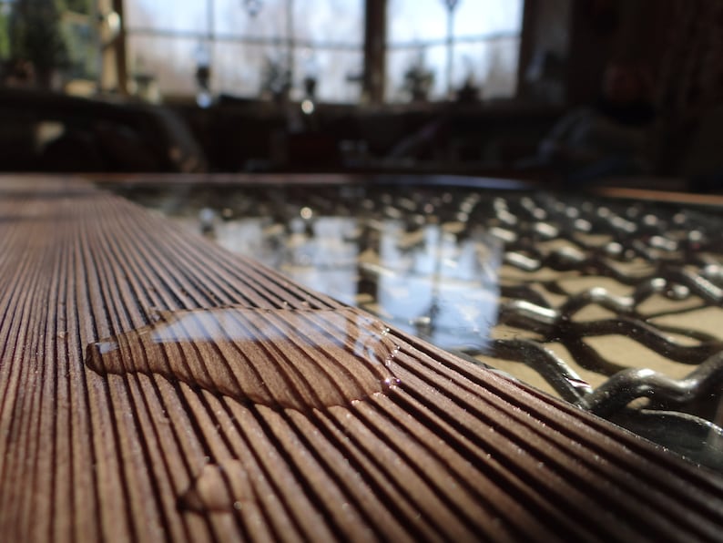 May include: A close-up of a wooden surface with a water droplet on it. The surface is made of thin, parallel strips of wood, creating a striped pattern. The water droplet is reflecting the light, creating a shimmering effect.