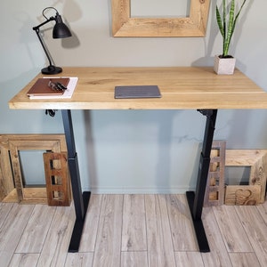 May include: A wooden standing desk with black adjustable legs. The desk has a light wood finish and is topped with a laptop and a notebook.