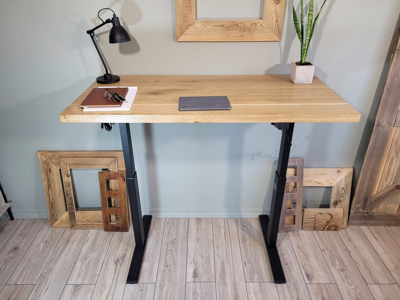 May include: A wooden standing desk with black adjustable legs. The desk has a light wood finish and is topped with a laptop and a notebook.