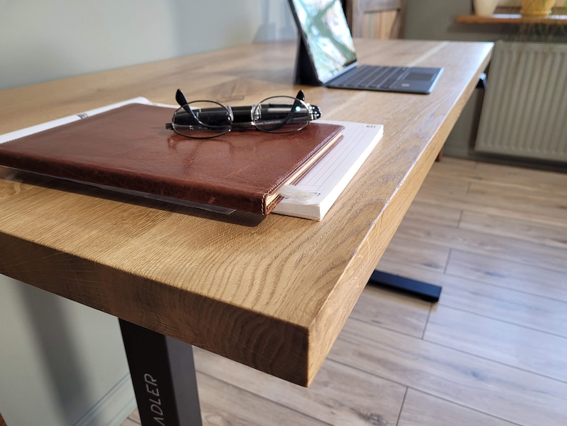 May include: A wooden desk with a brown leather-bound journal, a pair of glasses, and a pen on top. The desk has a black metal leg with the word "ADLER" printed on it.