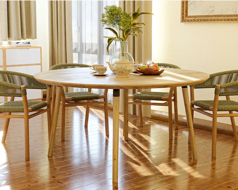 May include: A round wooden dining table with four chairs. The table has a light wood finish and the chairs have woven green seats and backs. There are green plants in a vase in the center of the table, along with a teapot and cups.
