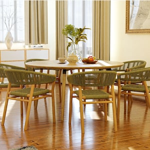 May include: A wooden dining table with six chairs. The chairs are made of woven green rope and have a natural wood frame. The table has a light wood finish and is set with a vase of flowers, a teapot, and a bowl of fruit.