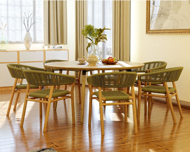 May include: A wooden dining table with six chairs. The chairs are made of woven green rope and have a natural wood frame. The table has a light wood finish and is set with a vase of flowers, a teapot, and a bowl of fruit.