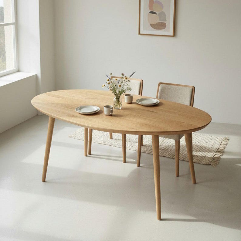 May include: An oval wooden dining table with four tapered legs. Two chairs with beige upholstered seats are positioned behind the table. The table is set with plates, mugs, and a vase of flowers. The table is approximately 72 inches long.