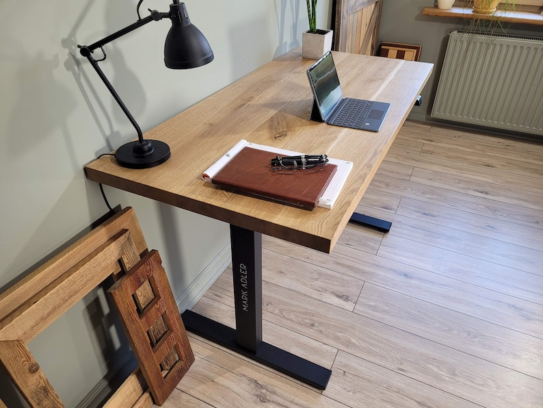 May include: A wooden desk with a black metal frame. The desk has a laptop, a notebook, and a lamp on it. The desk is in a room with wooden floors.