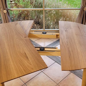 May include: A round wooden table with two leaves that extend out from the center. The table is made of light wood and has a natural finish. The leaves are attached to the table with metal hinges.
