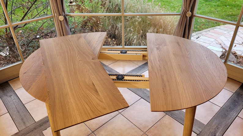 May include: A round wooden table with two leaves that extend out from the center. The table is made of light wood and has a natural finish. The leaves are attached to the table with metal hinges.