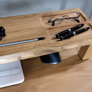 Op de afbeelding: Een houten bureau-organizer met een gleuf voor een potlood, twee vakken voor pennen en een klein vak voor brillen. De organizer is gegraveerd met de naam "Oliver Johnson".
