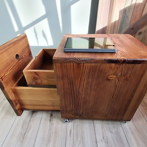 Pode incluir: Uma mesa de apoio de madeira com duas gavetas e uma superfície superior. A mesa é feita de madeira recuperada e tem um acabamento rústico. Um tablet está na superfície superior.