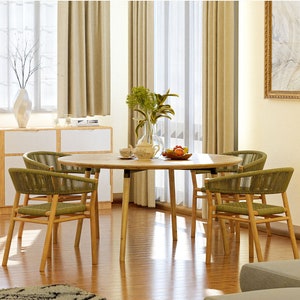 May include: A round wooden dining table with four chairs. The table and chairs are made of natural wood with a light brown finish. The chairs have green woven seats and backs. The table is set with a vase of flowers, a bowl of fruit, and a few plates and cups.