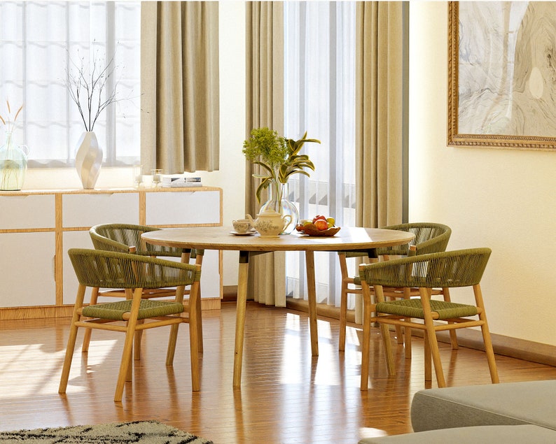 May include: A round wooden dining table with four chairs. The table and chairs are made of natural wood with a light brown finish. The chairs have green woven seats and backs. The table is set with a vase of flowers, a bowl of fruit, and a few plates and cups.