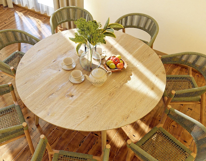 May include: A round wooden table with six green wicker chairs surrounding it. The table is set with a teapot, cups, saucers, and a bowl of fruit. The table is in a room with wooden floors and sunlight streaming through the windows.