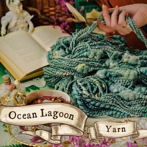 May include: Teal blue yarn with a textured, chunky look. The yarn is called "Ocean Lagoon Yarn" and is displayed on a table with a book and a cup of tea.