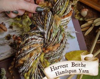 Pode incluir: Um novelo de fio fiado à mão Harvest Beithe numa mistura de cores incluindo verde, castanho, branco e laranja. O fio é segurado por uma mão com verniz verde. A imagem também inclui o texto "Wild Yarn".
